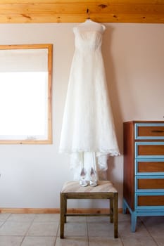 A wedding dress hangs in the bridal suite with wedding shoes before the bride gets ready.