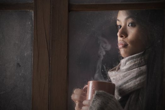 Portrait of a beautiful woman behind window with a cup of coffee or tea