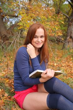 young, beautiful girl holding an open book, read background fall park