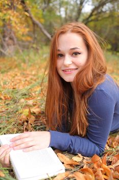 young, beautiful girl holding an open book, read background fall park