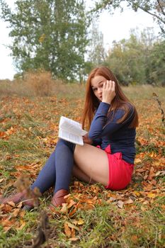young, beautiful girl holding an open book, read background fall park
