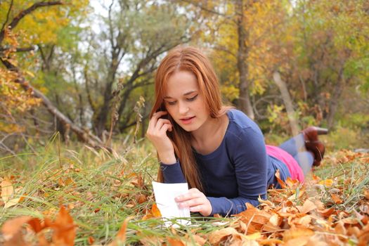 young, beautiful girl holding an open book, read background fall park