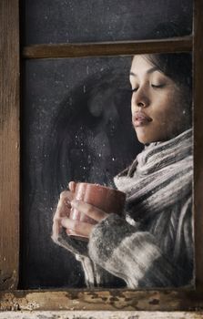 Portrait of a beautiful girl behind window with a cup of coffee or tea