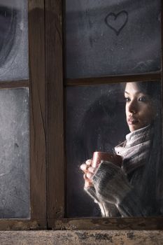 Portrait of a beautiful girl behind window with a cup of coffee or tea