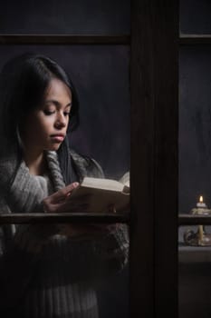 Portrait of a beautiful woman behind window reading a book 