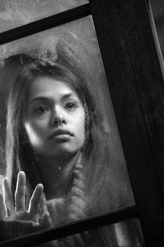 Portrait of a beautiful woman behind window, focus on rain drop