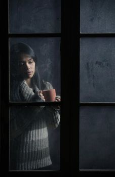 Portrait of a beautiful girl behind window with a cup of coffee or tea