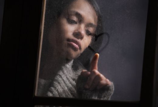 Portrait of woman drawing heart on wet window