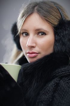 Young woman wearing winter clothes having a hot drink, shallow deep of field