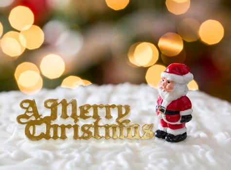 Santa on iced christmas cake with lights of xmas tree out of focus in background