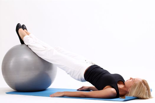 Young and beautiful woman doing exercise with fitness ball lying on a blue mat