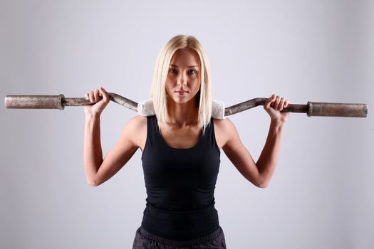 Slim and sporty young blonde doing fitness exercise with fitbar in studio