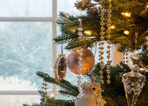 Macro shot of christmas tree decorations on indoor tree as snow falls outside window