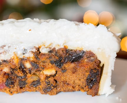Slice out of iced christmas cake with lights of xmas tree out of focus in background