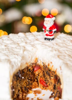 Slice out of iced christmas cake with lights of xmas tree out of focus in background