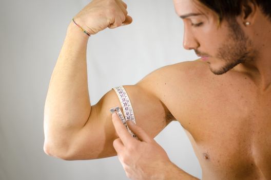 Athletic young man measuring biceps with tape meter