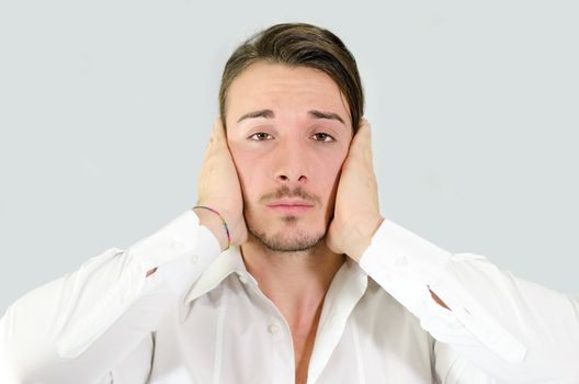 Depressed, sad or irritated young man covering ears with hands