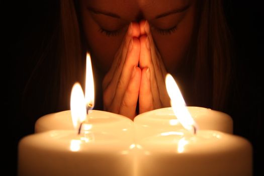 Young woman prays over alight candles in a darkness