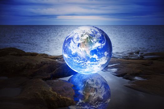 Conceptual image of a Glowing earth in a puddle at sea. Earth image provided by NASA.