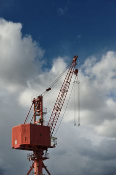 Red metal crane against cloudy sky