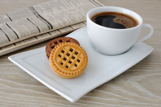 A cup of fresh brewed coffee and biscuits on the table with newspaper