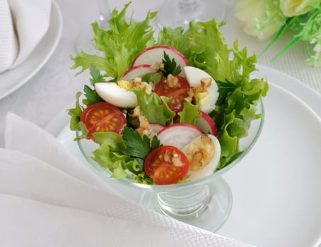 Salad of cherry tomatoes with quail egg and radish in the salad leaves