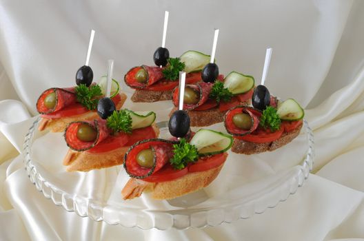 Sandwiches (canapés) of salami with olives on a plate