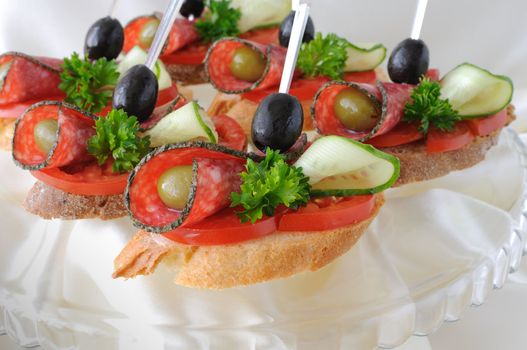 Sandwiches (canapés) of salami with olives on a plate