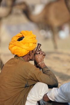 Man in orange turban smoking a clay pipe at the Pushkar Camel Fair in Rajasthan, India