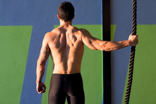 Crossfit gym man holding hand a climbing rope rear view