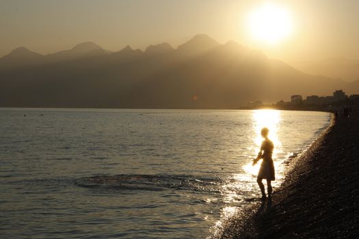 Young swimmer in rays of the setting sun ready to enter the water, Mediterranean Sea, Konyaalti beach, Antalya, Turkey