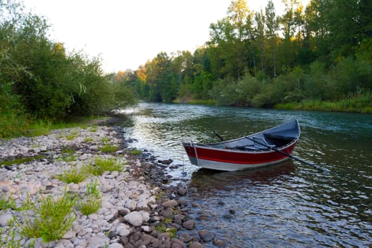 A red drift boat is anchored along the river bank during a day of floating and fishing.