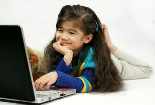 Little girl playing on her laptop on floor