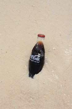 Fresh Coca-Cola in glass bottle in a sand at the tropical beach, Thailand