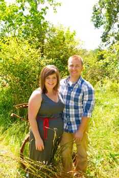 A man and a woman are in an overgrown field with rusted farm equipment.