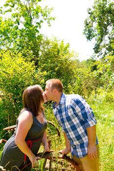 A man and a woman are in an overgrown field with rusted farm equipment.