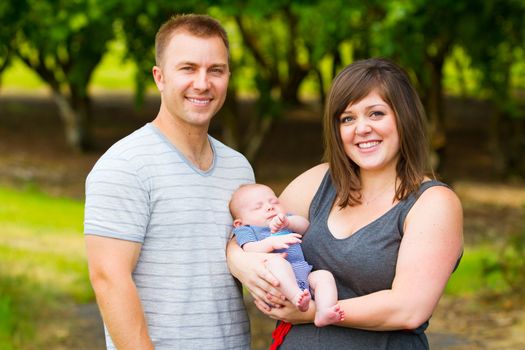 An attractive couple holds their newborn baby in their arms.