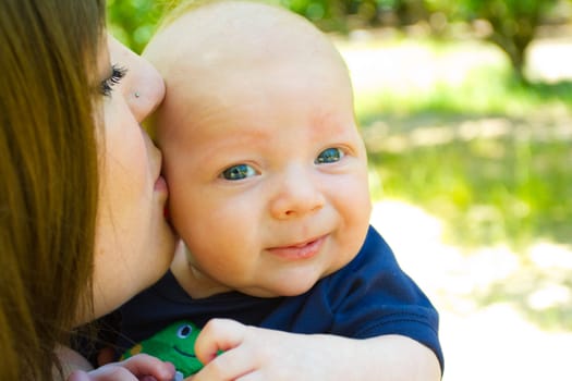 An attractive woman holds her newborn baby boy in her arms outdoors.