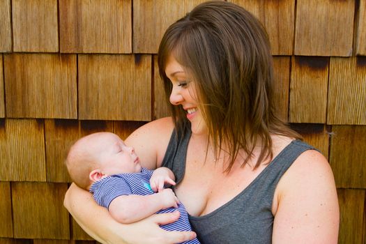 An attractive woman holds her newborn baby boy in her arms outdoors.