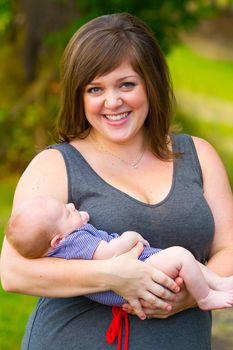 An attractive woman holds her newborn baby boy in her arms outdoors.