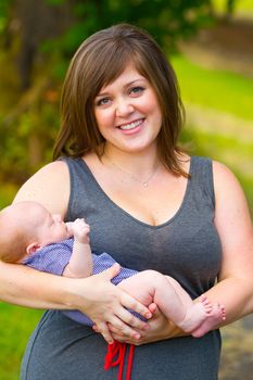 An attractive woman holds her newborn baby boy in her arms outdoors.