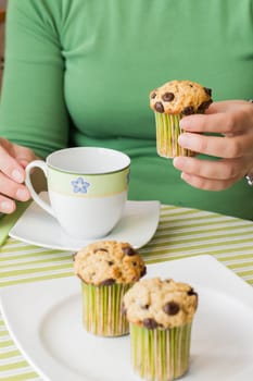 Nice girl hand taking delicious chocolate chip muffin at breakfast in green striped tablecloth