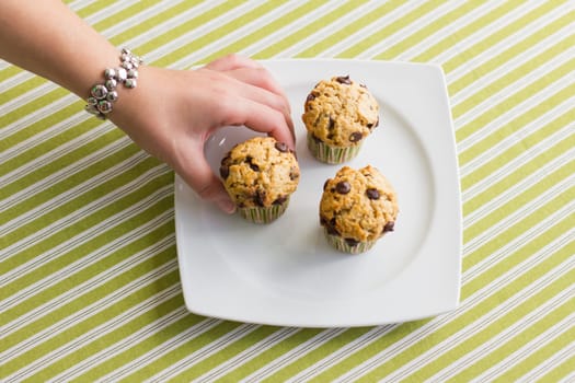 Nice girl hand taking delicious chocolate chip muffin at breakfast in green striped tablecloth