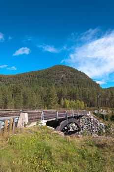 Old wooden bridge over the river on a background of mountains