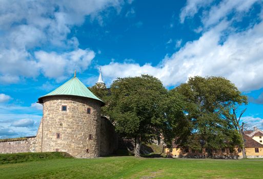 Castle tower with residential buildings and trees against the sky with clouds