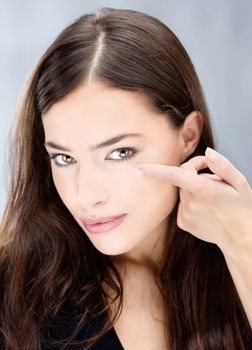 Young brunette woman holding contact lens on finger in front of her eye