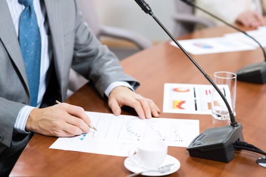 Businessman writing on paper notes, On the table is a cup of coffee and a device for communication at the conference