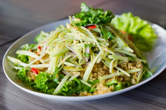 spicy crispy catfish salad with green mango and fresh vegetable on white plate