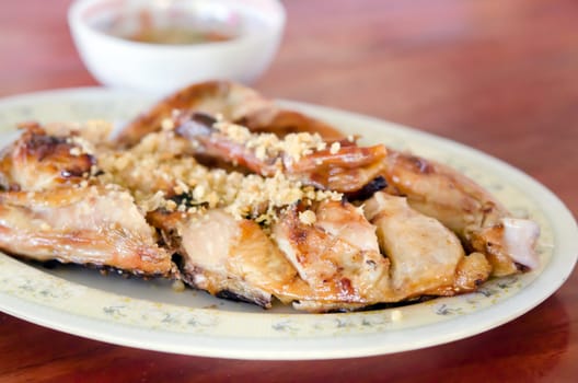 Grilled chicken with fried garlic on dish served with spicy sauce in bowl