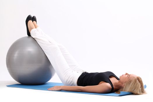 Young and beautiful woman doing exercise with fitness ball lying on a blue mat